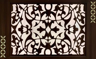 Close up of random ethnic ornamental swirls decoration carved on a black panel. Classic ornamental decoration with backlight on white acrylic and floral pattern. Seamless background texture.