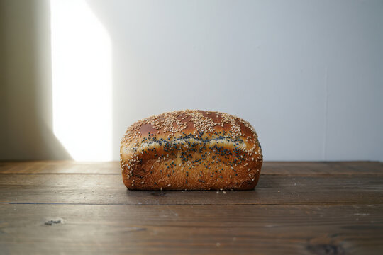 A loaf of multigrain bread with sesame seeds on a wooden table with natural light