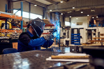 Welder Wearing Protective Gear Working on Metal Parts in a Bright Workshop