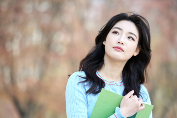 Fototapeta premium Young Asian female student holding books outdoors in springtime park 