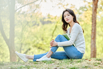 Obraz premium Young Asian female relaxing and reading a book outdoors in spring park