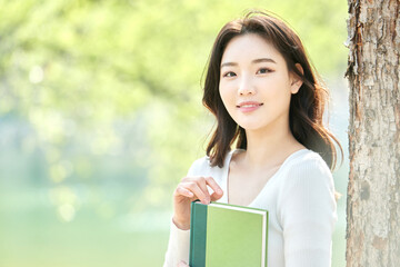 Fototapeta premium Young female reading book outdoors in spring leaning against tree