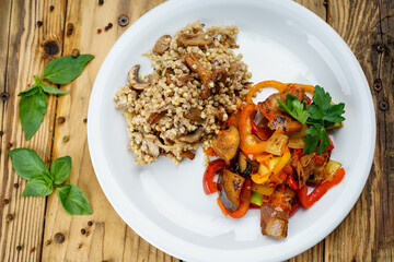 Porridge with mushrooms and stewed eggplant with vegetables in a white plate on a background