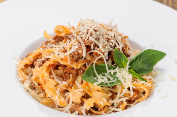 pasta with meat and cheese and basil in a white plate on a wooden background macro photo