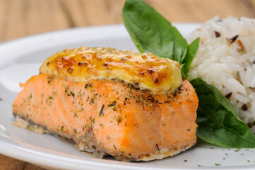 rice with salmon fillet under cheese in a white plate on a macro background