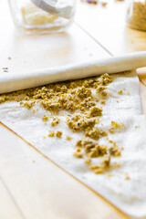 A close-up of the culinary process of making baklava: a thin sheet of filo dough lies on a wooden table, and a hand carefully sprinkles it with chopped nuts. Golden-brown nut crumbs are evenly