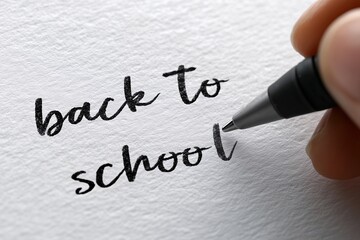 Hand writes back to school in cursive with black pen on textured white paper