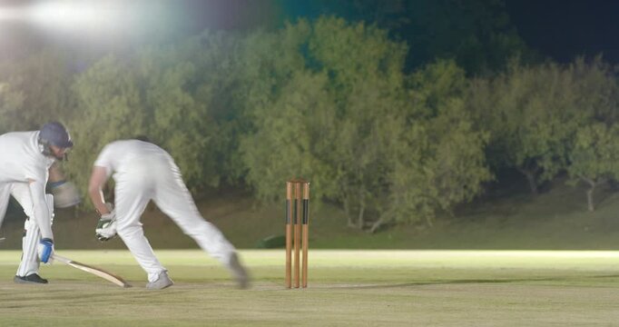 On delivery, Indian batsman playing shot defending wicket on pitch at night while keeper retrieving
