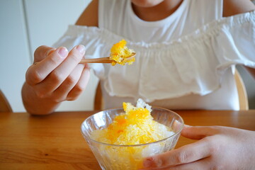 Enjoying homemade mango shaved ice with additive-free syrup, a wooden spoon lifting fluffy ice while bright citrus color glows in a clear glass bowl