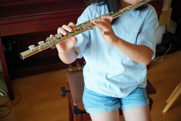 Close-up of a child practicing the silver flute at home, fingers on the keys during a relaxed music lesson © リリ