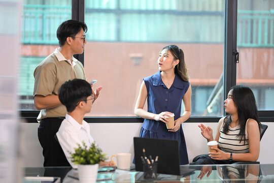 Office colleagues take a break from work to relax and chat with coffee cups in hand - Powered by Adobe