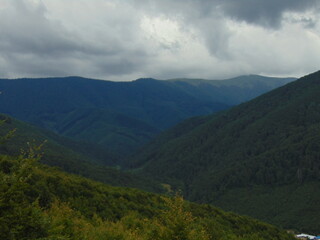 Rolling green mountains stretch into the distance under a dramatic cloudy sky, creating a peaceful yet powerful scene of untouched natural beauty and wilderness