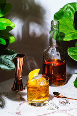 Special Old fashioned alcoholic cocktail drink with tequila, soda, ice and lemon twist. Marble table in elegant lounge bar with green plants