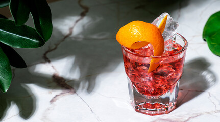Tegroni, alcoholic cocktail drink with tequila, red bitters, sweet vermouth and orange peel. Marble table in lounge bar with green plants