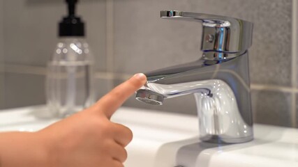 Child's Hand Pressing Chrome Faucet in a Modern Bathroom with Gray Tile Background - Powered by Adobe