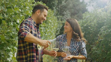 Winemakers pouring and tasting white wine in vineyard during sunny day
