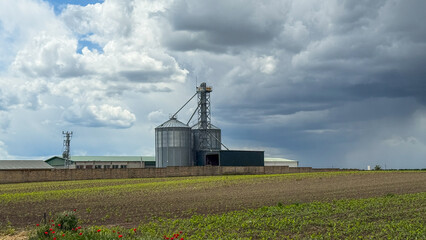 Obraz premium Storm clouds brood over a solitary grain silo, embodying Harvest Festival tension and agrarian lore's silent whispers