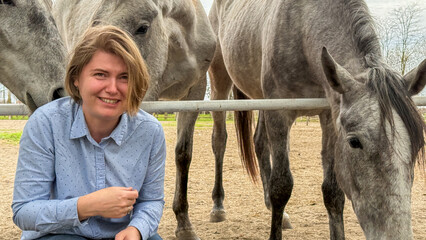 Smiling Caucasian woman amidst charismatic grey horses, evoking equestrian camaraderie, Earth Day...