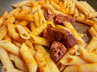 Penne pasta with meat and spices cooking in a pan