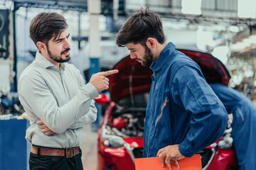 Angry customer pointing at car mechanic in busy workshop about repair problem and warranty claim, highlighting service dispute, complaint handling, and automotive repair conflict situation.