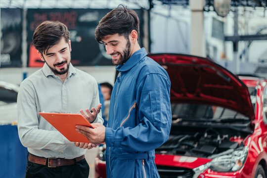 Happy car owner discussing repair and maintenance with mechanic beside red car, representing trust, quality service, and positive customer experience in automotive workshop.