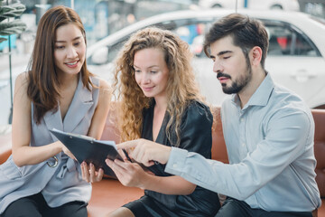 Young couple reviewing car purchase agreement with female sales agent, showing consultation, attention to detail, and trusted service in automotive sales and customer relations.