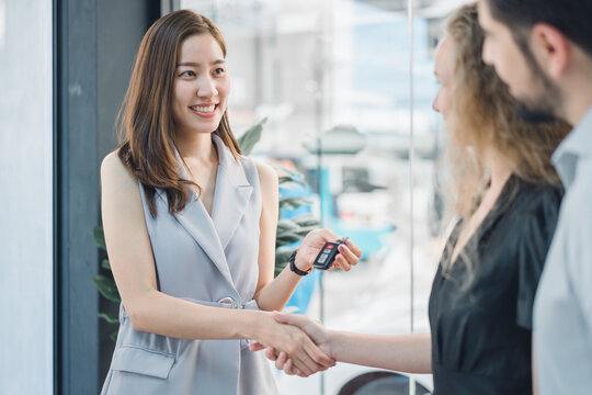 Professional female car dealer shaking hands and giving keys to smiling customer, symbolizing trust, joy, and success in automotive purchase and customer relations.