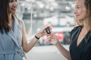 Car dealer handing new keys to happy female customer in showroom, showing successful purchase, trust, and satisfaction in automotive sales and finance.
