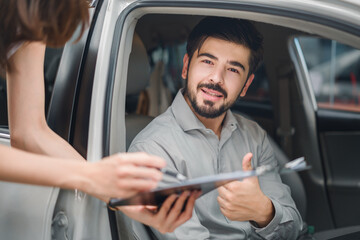 Happy customer in new car giving thumbs up while sales agent holds clipboard, symbolizing trust, professional service, and success in automotive sales transaction.