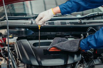 Obraz premium Mechanic checking engine oil level with dipstick in workshop, representing detailed inspection, professional service, and reliability in automotive maintenance industry.