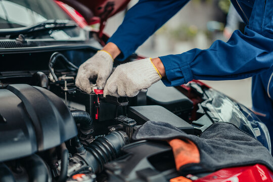 Mechanic inspecting and tightening battery terminal in workshop, representing professional service, quality check, and safety in automotive maintenance industry.