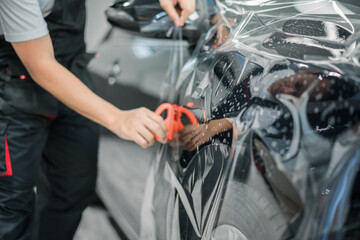 Car service worker applying transparent film on new car door, symbolizing careful detailing, paint protection, and premium automotive maintenance services.