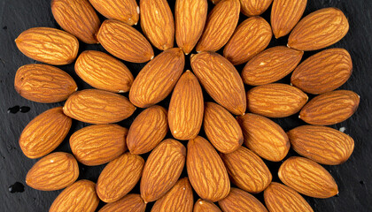 Fototapeta premium Almonds arranged in a circular pattern on a dark, textured surface.