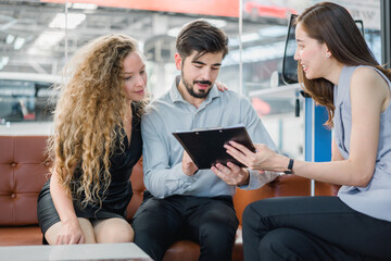 Couple reviewing purchase agreement on tablet with sales agent in showroom, representing modern buying experience, trust, and satisfaction in automotive sales.