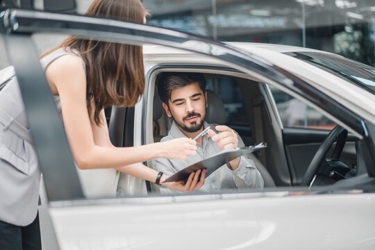 Male customer in new car signing purchase agreement with female sales agent, representing trust, professionalism, and success in automotive sales.