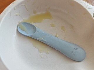 First solid food experience with homemade organic mashed potato and olive oil on baby plate with tiny blue spoon