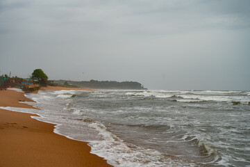 A tranquil coastal view of a pristine beach in Goa, India, captured during the monsoon season. Golden sand meets the foamy waves of the Arabian Sea under a soft blue sky
