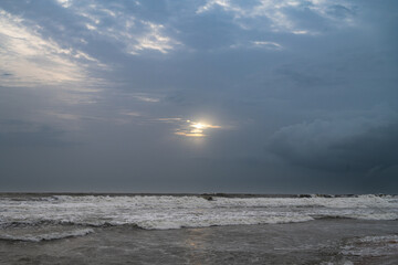 A tranquil coastal view of a pristine beach in Goa, India, captured during the monsoon season. Golden sand meets the foamy waves of the Arabian Sea under a soft blue sky