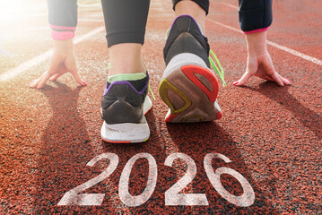 Starting with the new year 2026. a woman prepares to start on an athletics track engraved with 2026. the idea of planning, goals and new year resolutions.