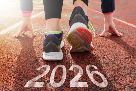 Starting with the new year 2026. a woman prepares to start on an athletics track engraved with 2026. the idea of planning, goals and new year resolutions.