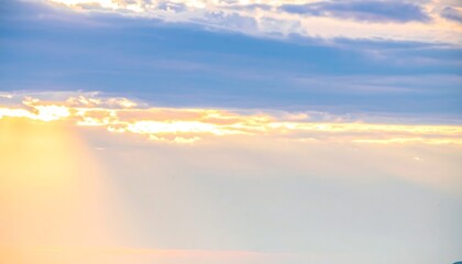 Sunbeams pierce through a partly cloudy sky at sunset, creating a warm, hazy glow