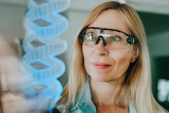 Scientist wearing protective eyewear observing DNA strand in laboratory - Powered by Adobe