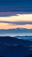 Obraz premium Serene sunrise over a vast, layered mountain range, with subtle pastel hues in the sky