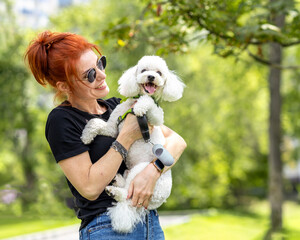  A young woman plays with a white poodle in the park.