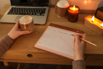 Close-up of a cozy desk scene with a person holding a glass of coffee in one hand and a golden pen...