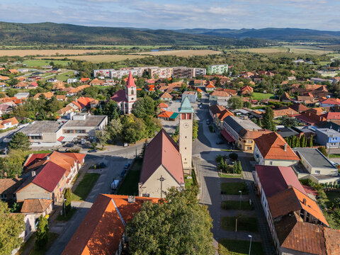 Aerial view of the church tower rising amidst the village's red-roofed buildings, framed by distant hills, Pukanec, Nitra Region, Slovakia.