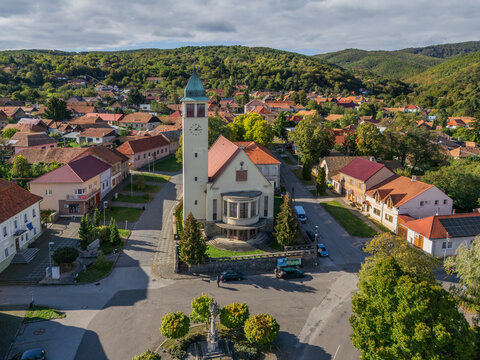 Aerial view of a church standing tall amidst a quaint village nestled in the undulating hills, with a charming blend of nature and architecture, Pukanec, Nitra Region, Slovakia.