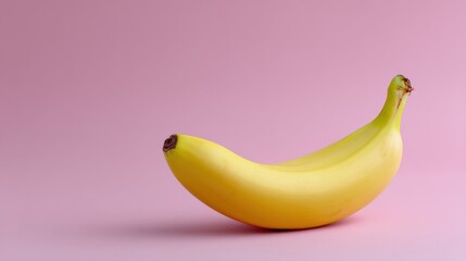 Close-up of a single banana on a pink background. the banana is yellow in color and has a curved shape with a small brown spot on the top.