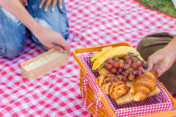 Friends enjoying picnic with croissants, grapes and bananas in park