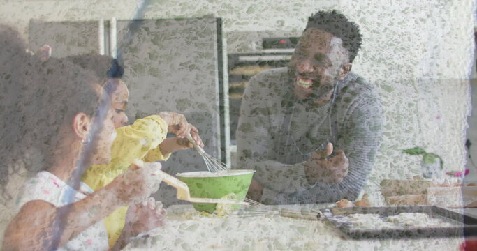 Mixing father and children stirring batter at kitchen island, with green mixing bowl and pastries